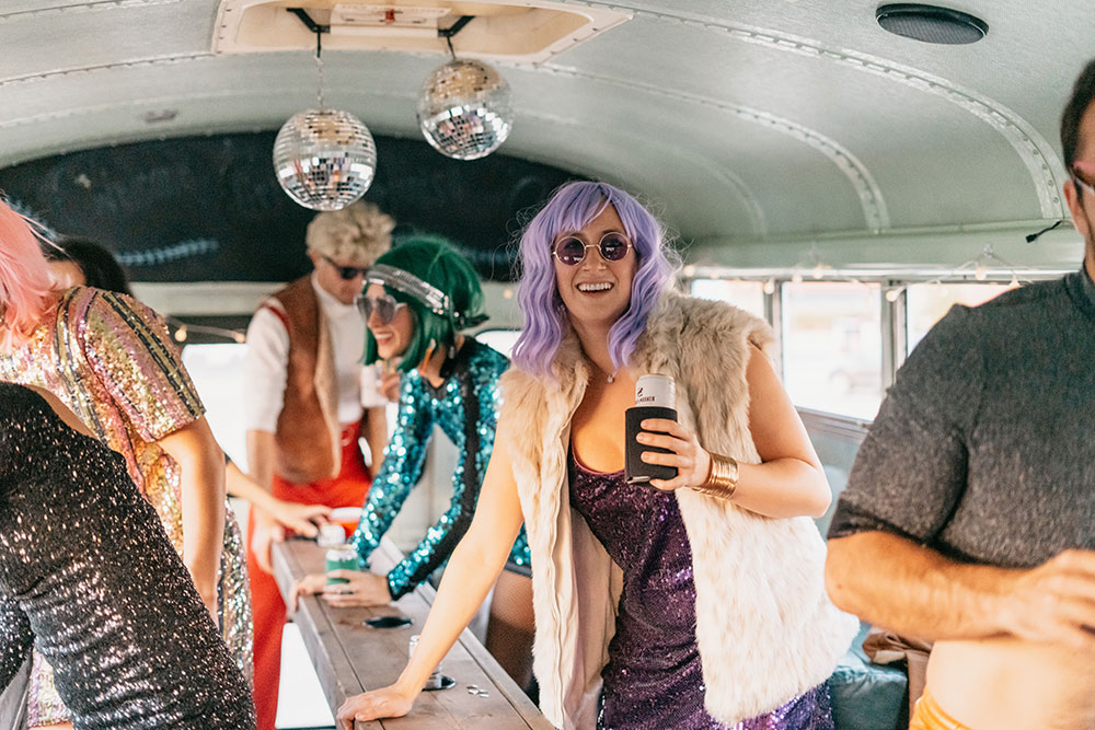 Guest in a purple wig and sequins beside the party bus table
