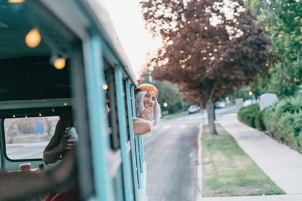 Guest smiling out the window of the teal party bus on a Boise street